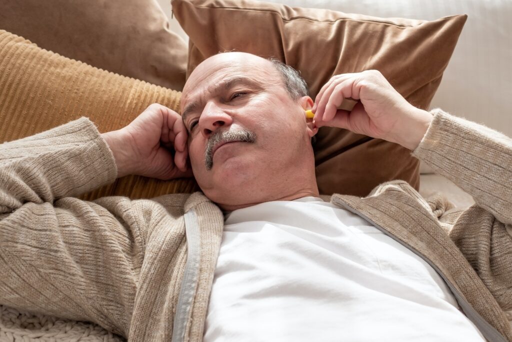 Senior stressed man holding a yellow earplug trying to sleep having insomnia