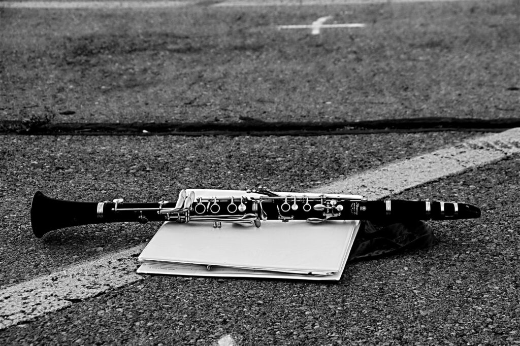 Monochromatic image of clarinet lying on a white binder in a high school parking lot.